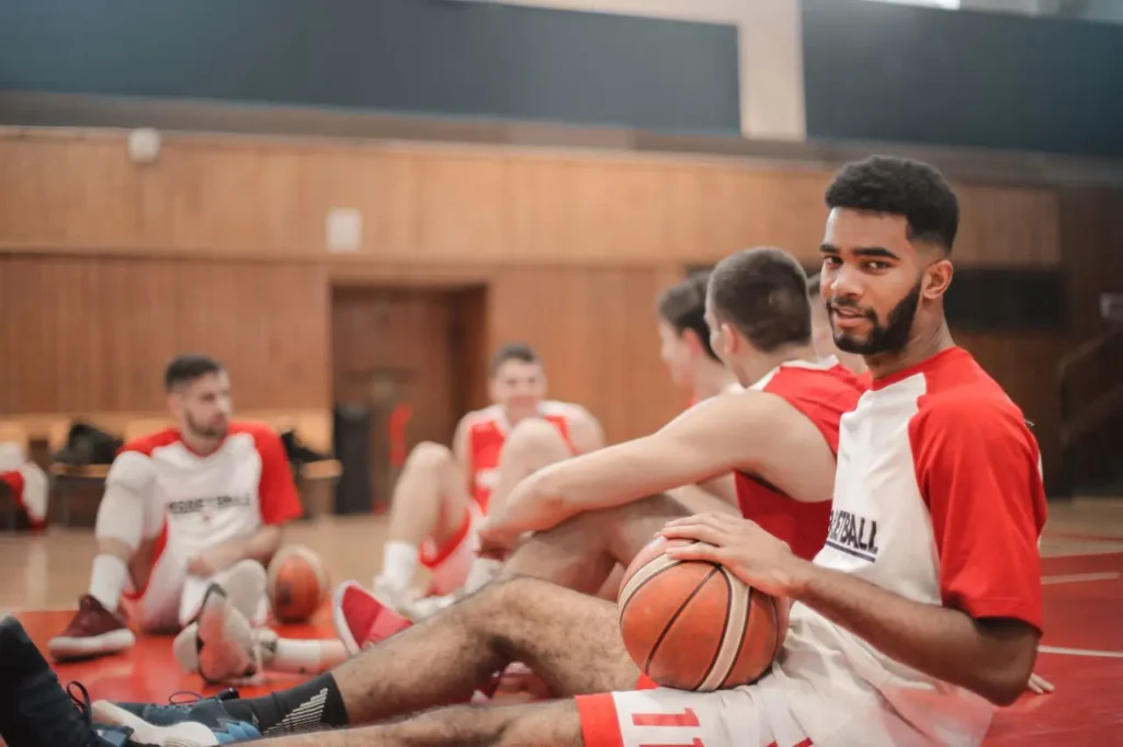 basketball player sits on the gym floor holding a basketball while